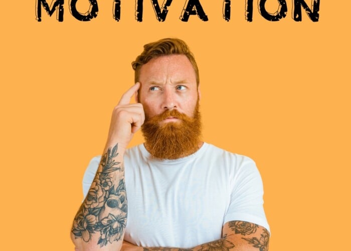 Orange background. In the center taking up most of the picture is a white man in a white shirt with red hair, a red beard, and tattoos on both arms. You can see him from just above his waist up. Above him is the word motivation. The man has h is finger to his temple to demonstrate he's thinking. It's supposed to signify trying to understand intrinsic vs extrinsic motivation and what they are.
